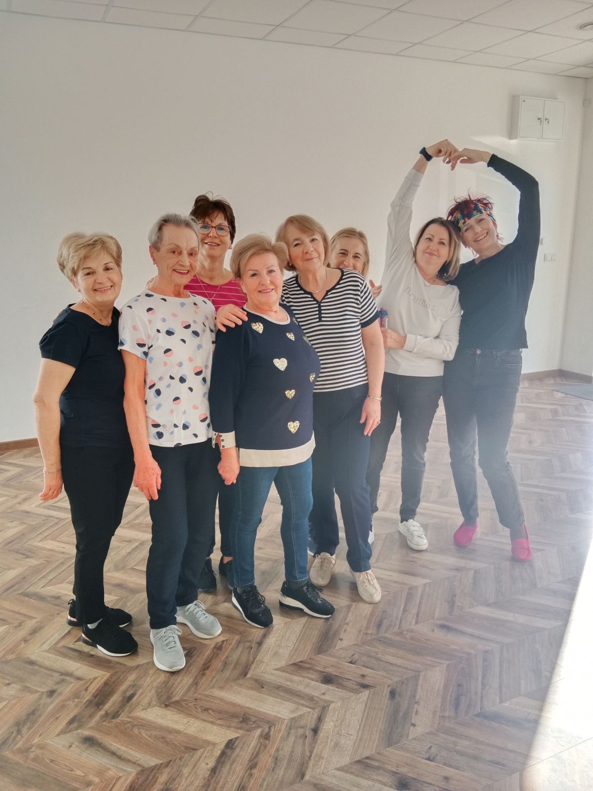 Uśmiechnięte seniorki pozują wspólnie po zakończonych zajęciach w sali.