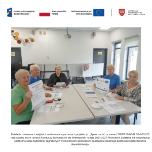 Świetlica wiejska w Jasinie. Pięć uczestniczek zajęć, seniorek, siedzi przy dwóch zestawionych stołach. Dwie z nich pokazują plakaty projektowe.