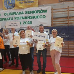 Zdjęcie przedstawia grupę swarzędzkich seniorów podczas olimpiady dla seniorów w Luboniu. Stoją z dyplomami przed banerem.