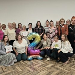 Na zdjęciu grupa uczestniczek Klubu Kobiet z nadmuchanym balonem - cyfrą 2 stoją lub kucają uśmiechnięte do zdjęcia.