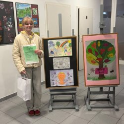 Zdobywczyni drugiego miejsca. W prawej ręce trzyma torebkę z nagrodami, a w lewej ręce dyplom. Obok widać nagrodzone prace.