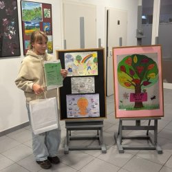 Zwyciężczyni konkursu plastycznego pod tytułem Moja moc w trudnym czasie, jak dbam o zdrowie psychiczne. Dziewczynka stoi obok sztalug ze zwycięskimi pracami.