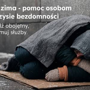 Zdjęcie przedstawia prawdziwego bezdomnego mężczyznę śpiącego na ośnieżonym kartonie położonym na chodniku. Mężczyzna jest przykryty kocem.