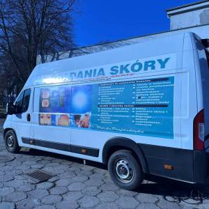 Zdjęcie przedstawia zbliżenie na busa typu transporter, w którym przeprowadzane są badania skóry. W tle widać drzewo, budynek cusu i błękit nieba.