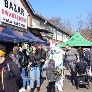 Na zdjęciu widać namioty i stanowiska kół gospodyń wiejskich, chodzących ludzi i zająca maskotkę rozdającego dzieciom słodycze.