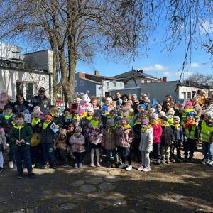 Zdjęcie grupowe wykonane w Ogrodzie Społecznym przy ulicy Poznańskiej. Widać na nim uczestników: dzieci, seniorów, panie opiekunki i rodziców.