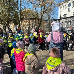 Ogród Społeczny. Grupa przedszkolaków z opiekunkami utworzyła krąg dokoła zająca maskotki i gitarzysty.