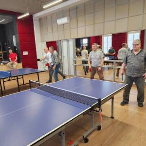 Sala na piętrze w Centrum Aktywności Seniora. Przy dwóch stołach do tenisa stołowego trwają dwa mecze. Wszystko odbija się w ścianie luster do fitnessu.