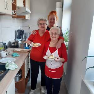 Trzy seniorki pozują do zdjęcia w kuchni trzymając talerze z wypiekami