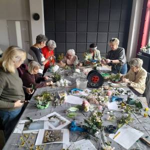 Seniorki pracują przy dużym stole nad florystycznymi dekoracjami