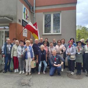 Zdjęcie przedstawia dwadzieścia pięć osób - uczestniczek i uczestników gry terenowej stojących przed wejściem do siedziby Dziennego Domu Senior Wigor.