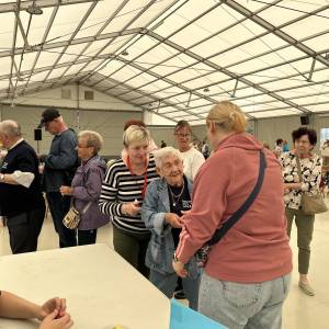 Namiot Sceny nad Jeziorem. Seniorki i seniorzy czekają na swoje konkurencje. Na pierwszym planie jedna z seniorek odbiera karnet.