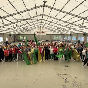 Pozowane zdjęcie grupowe ukazujące wszystkich uczestników korowodu stojących w namiocie Sceny nad Jeziorem. Wielu z nich trzyma w rękach z kolorowe flagi.