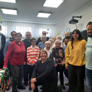 Zdjęcie grupowe w Dziennym Domu Pomocy. Wolontariuszka z Francji stoi w otoczeniu seniorów, pracowników i koordynatora projektu.