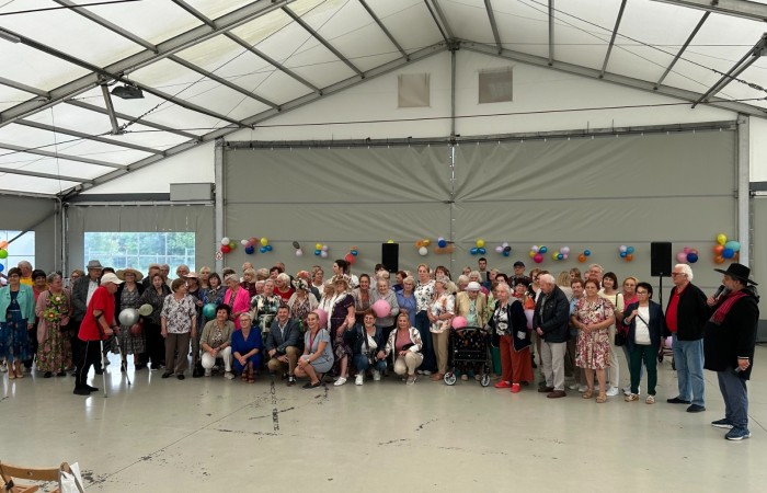 Zdjęcie grupowe wykonane wewnątrz namiotu przed Sceną nad jeziorem przedstawiające uczestników pierwszej w tym roku letniej dyskoteki dla seniorów.