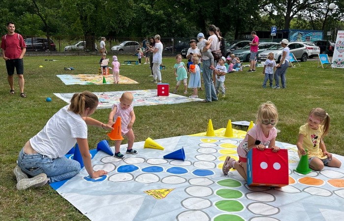Śniadanie na trawie. Na trawniku widać rozłożone gry wielkoformatowe, a przy nich i na nich graczy - dzieci i dorosłych.