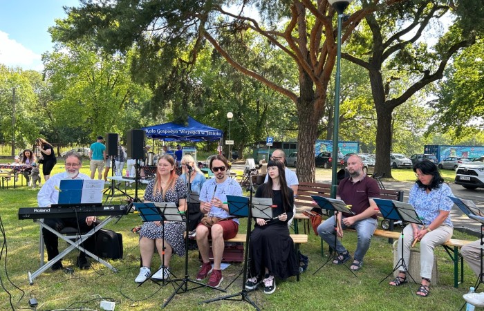 Śniadanie na trawie. Na trawniku pod sosną siedzą członkowie Swarzędzkiej Orkiestry Flażoletowej. Pierwszy z lewej przy klawiszach widoczny nestor polskiej muzyki flażoletowej Wojciech Wietrzyński.