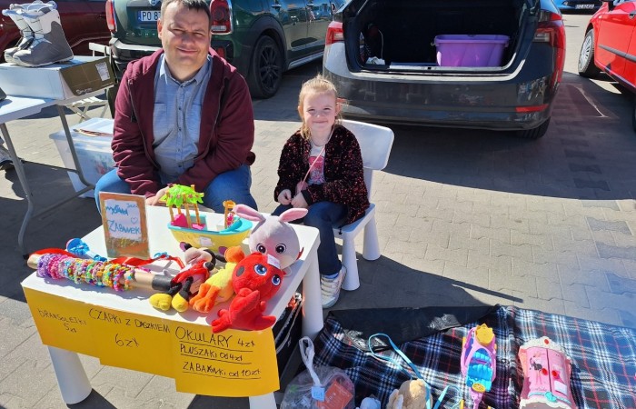 mezczyzna oraz dziewczynka za stolem z przedmiotami na sprzedaz