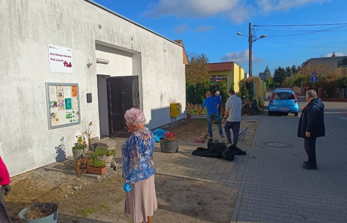 Na zdjęciu znajdują się osoby w wieku 60+ oraz instruktor zajęć, którzy wspólnie pracują nad ogródkiem Klubu Młodych Duchem Pod Lasem